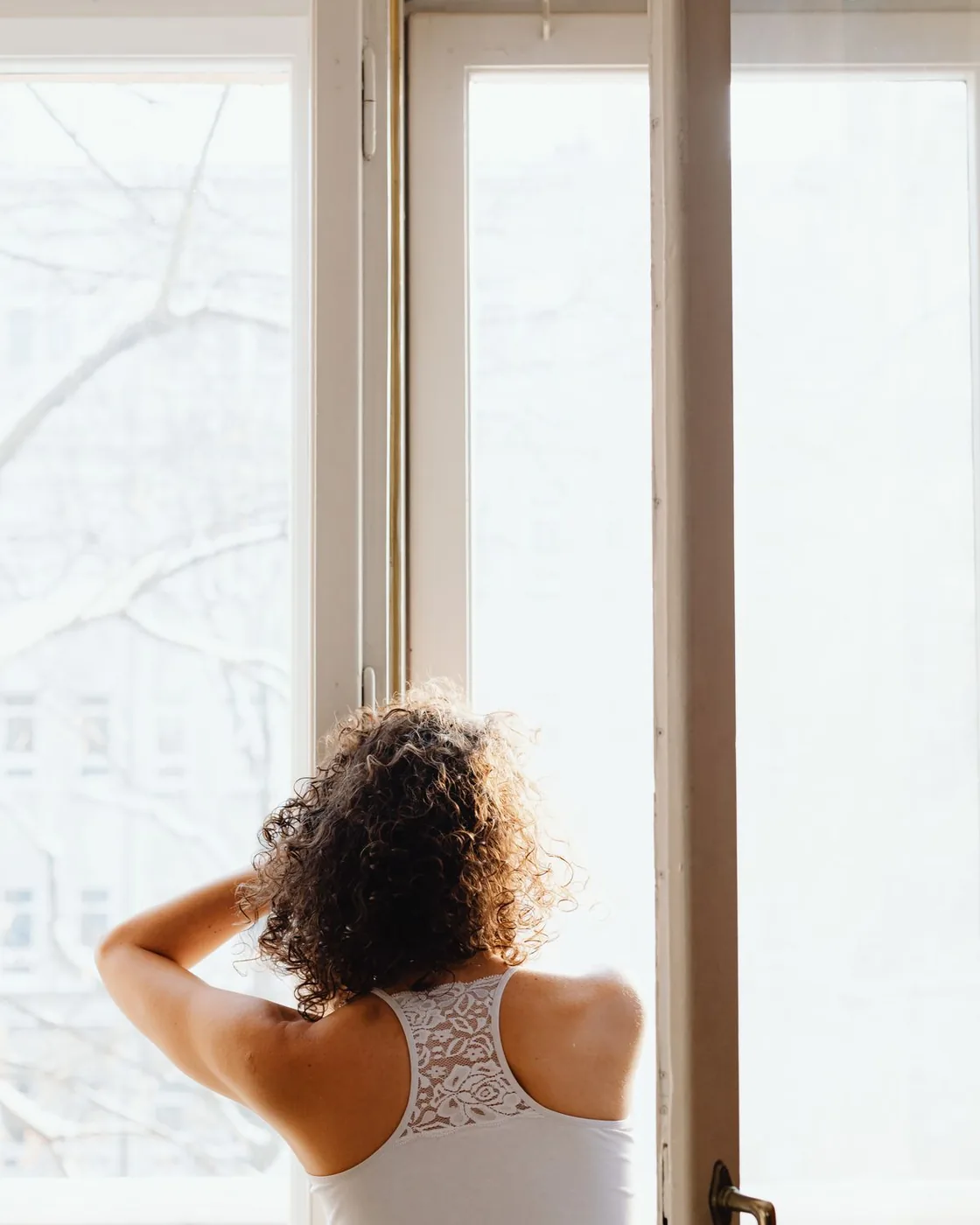 Una mujer de espaldas frente a una ventana abierta, con luz de la mañana